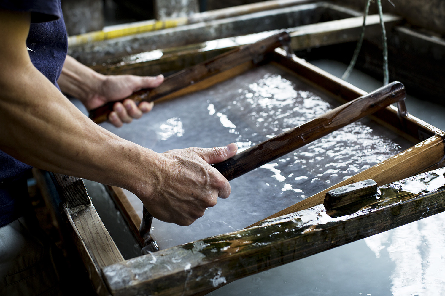 Washi. Foto de artesão fazendo um papel artesanal com bastidores de madeira em água.
