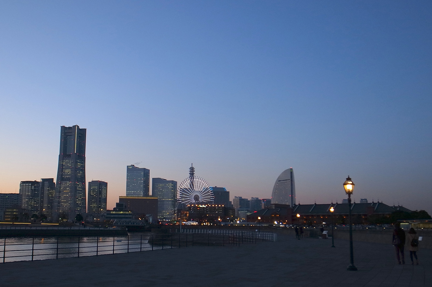 Minato Mirai, vista da cidade portuária de Yokohama com prédios no horizonte em pôr do sol, com céu azul. 