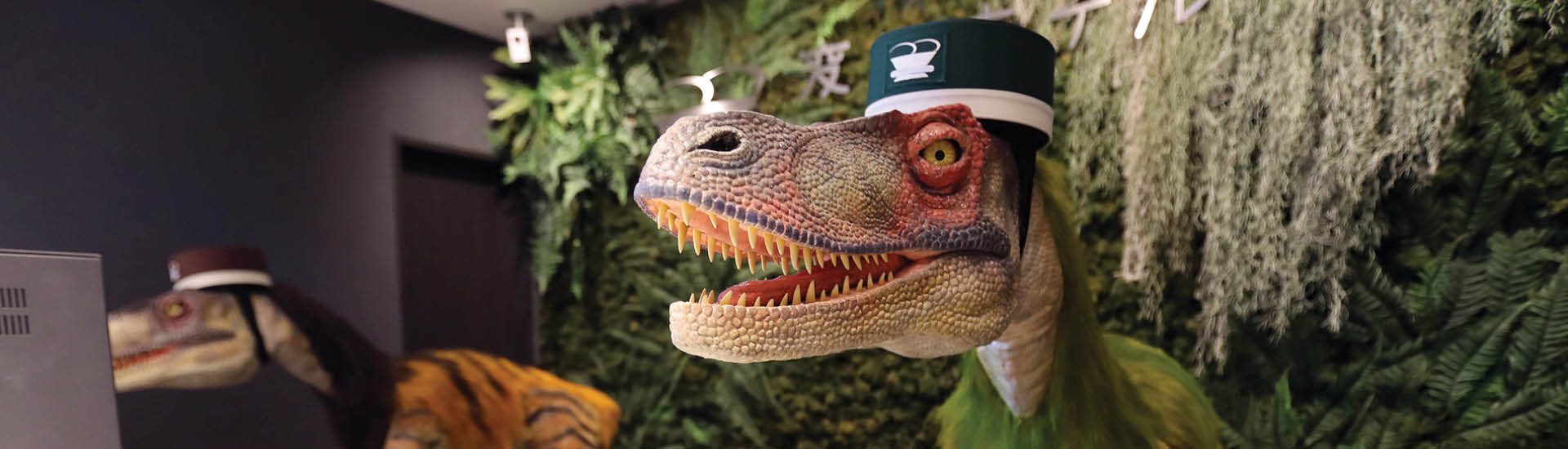 Dinossauros-robôs com quepe verde recepcionam hóspedes em hotel japonês.