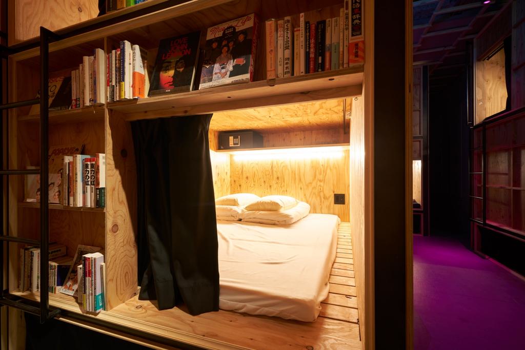 Quarto de hotel com uma cama entre prateleiras de madeira repletas de livros.