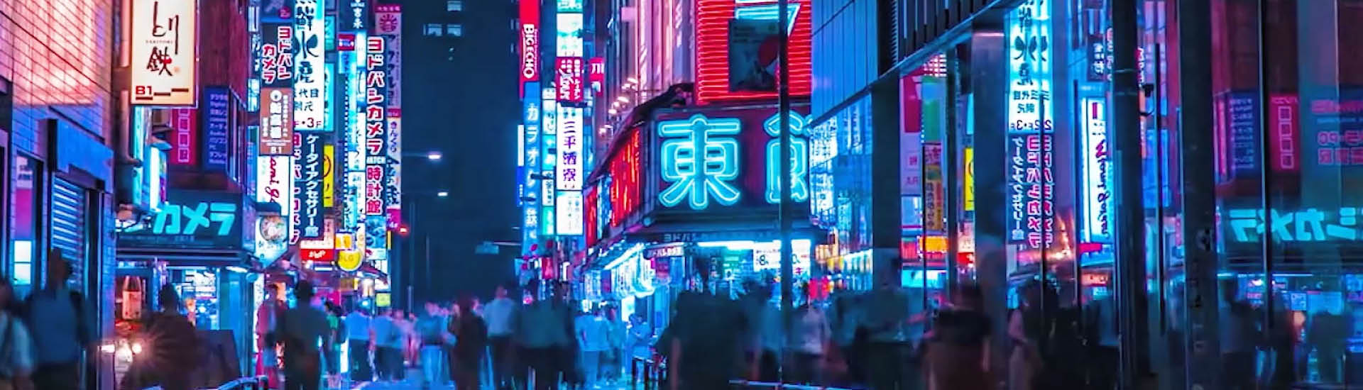 Cena noturna de cidade bem iluminada por diversos painéis com luz neon, com pessoas caminhando pelas ruas.