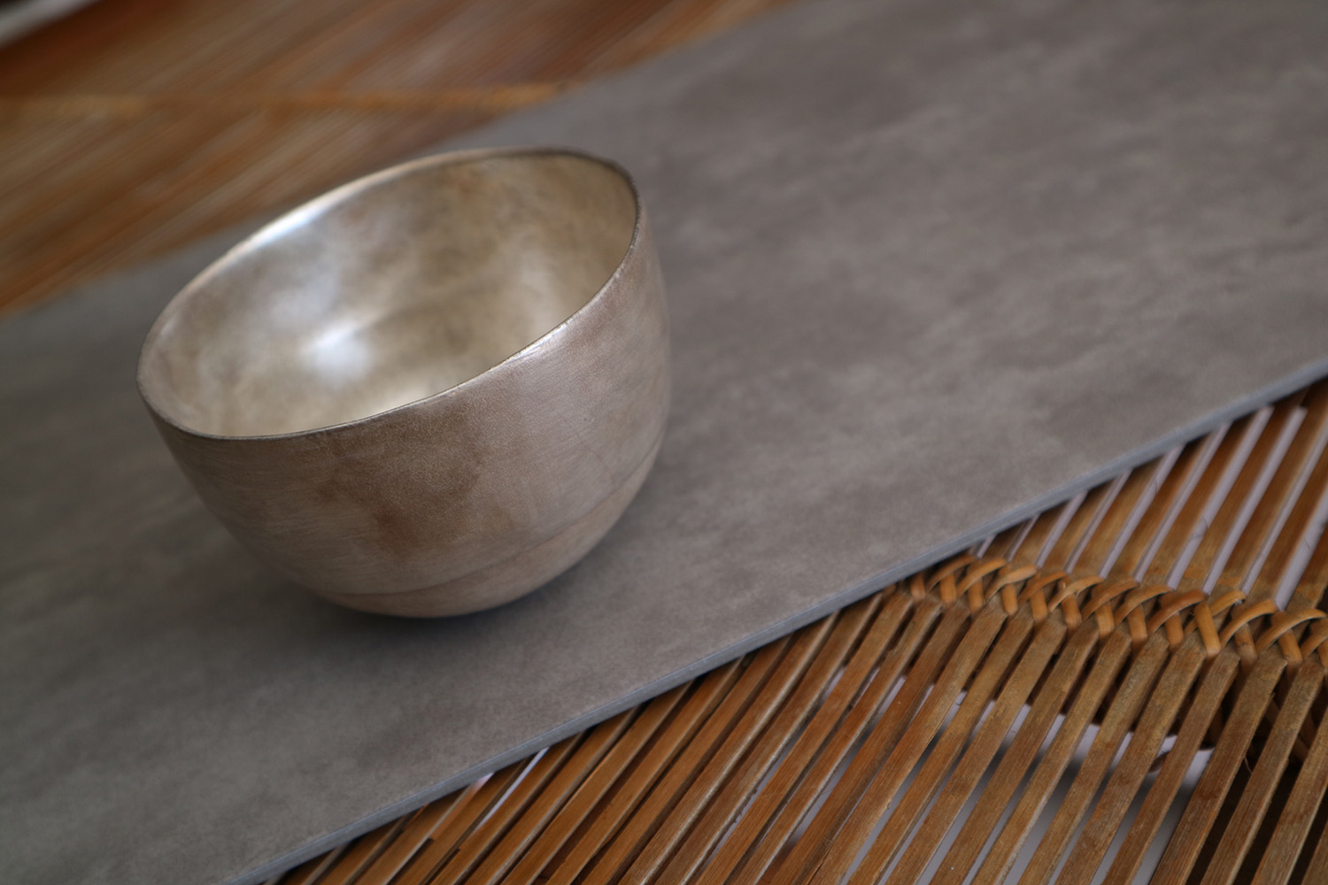 Pote de cerâmica com esmalte prateado em cima de tecido cinza sobre palha de madeira marrom.