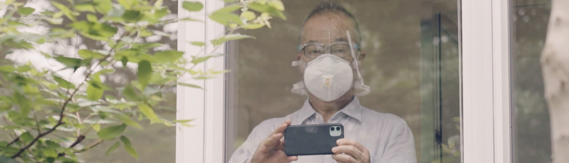 Hiroshi Yoda olha através de janela de vidro segurando um celular para fotografar.