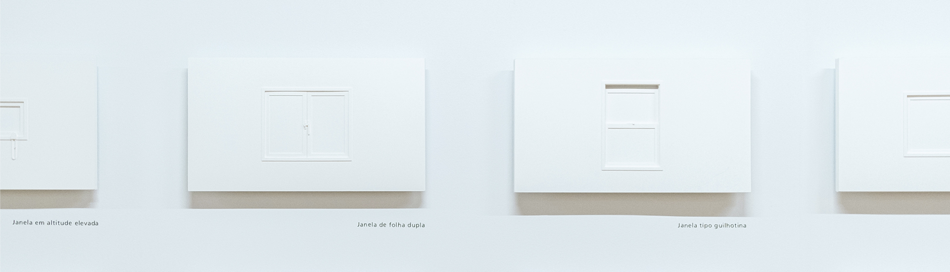 Pequenas janelas de papel branco, fixadas lado a lado em parede branca, na exposição 'WINDOWOLOGY: Estudo de Janelas no Japão'.