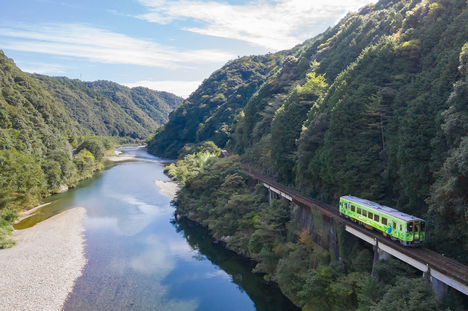 Trem percorrendo uma rota na beira de uma montanha com um rio ao lado.