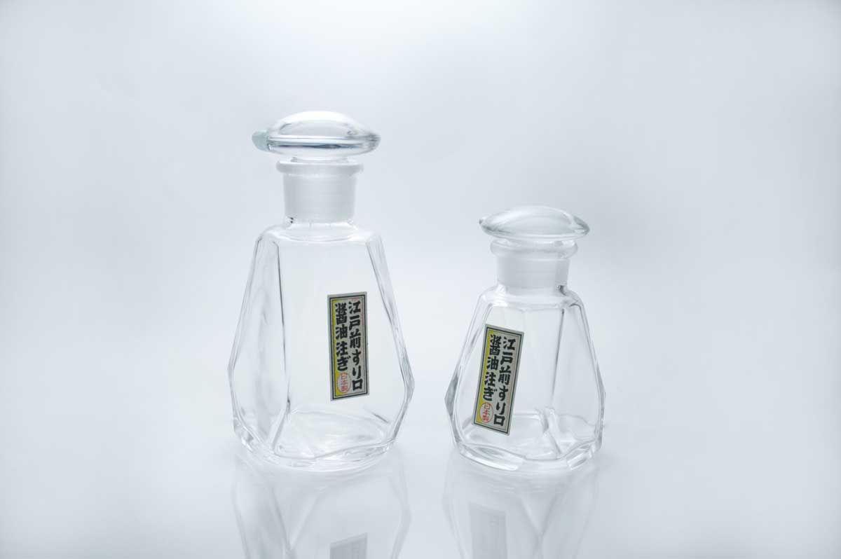 Foto de dois recipientes para shoyu em vidro transparente em fundo branco.