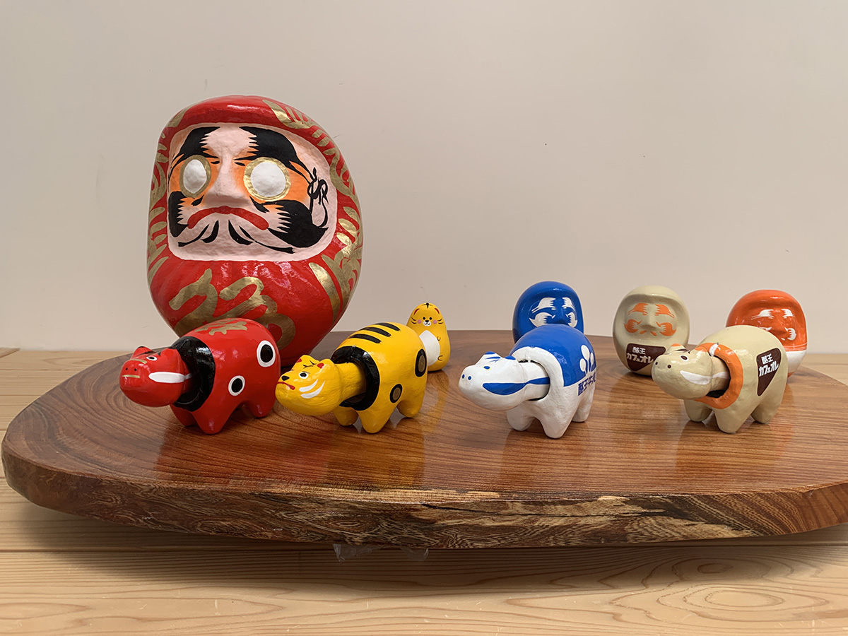 Daruma e outros bonecos miniatura coloridos sobre placa de madeira.