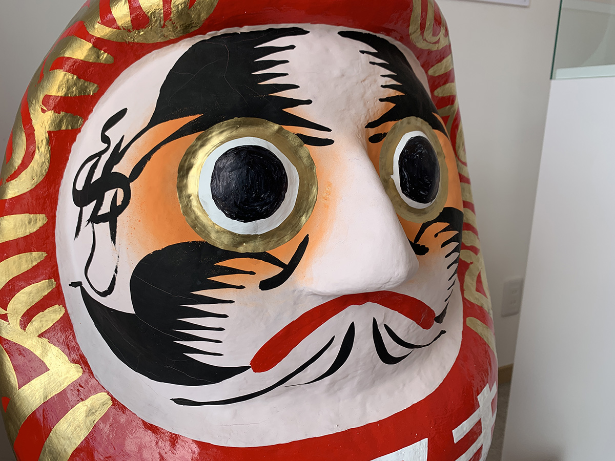 Daruma, boneco da sorte japonês, pintado de vermelho, preto e detalhes amarelos.