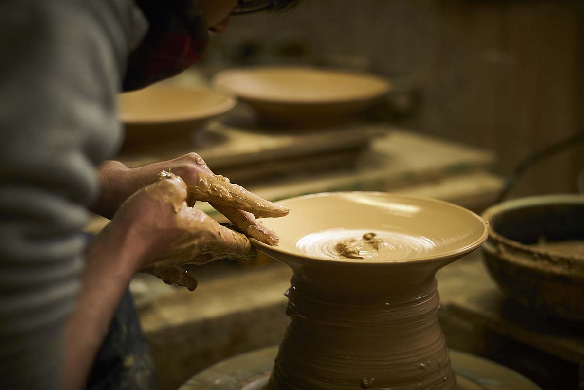 Foto aproximada das mãos do ceramista confeccionando a peça em cerâmica