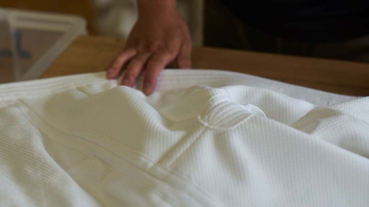 Imagem colorida de um tecido branco sendo tocado por uma mão