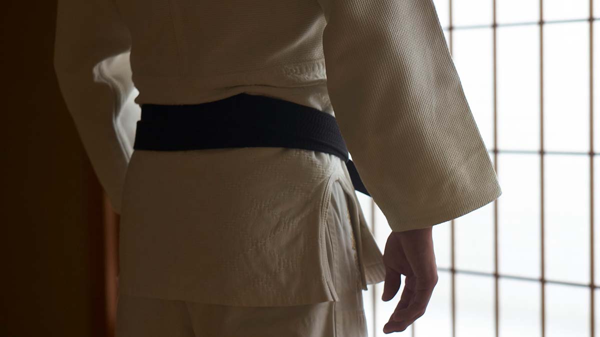 Imagem colorida de uma pessoa de costas vestindo um judogi branco com uma faixa preta 