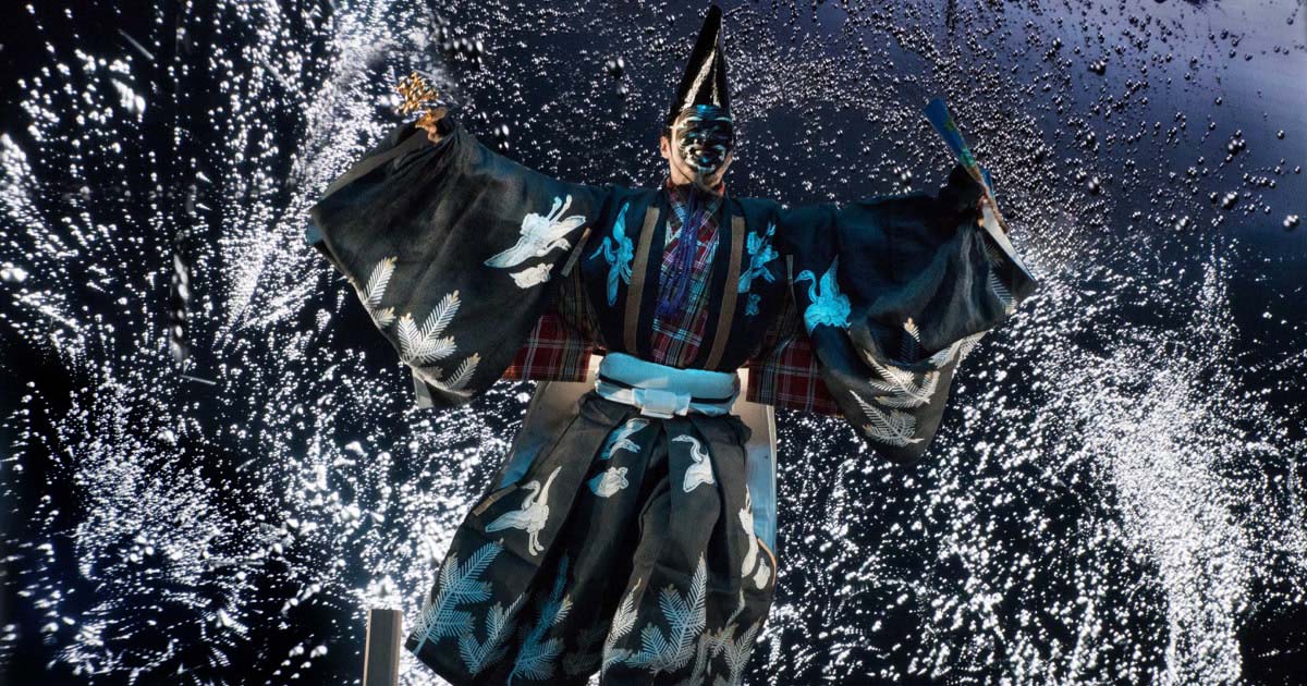 Artista em performance vestindo quimono e máscara 