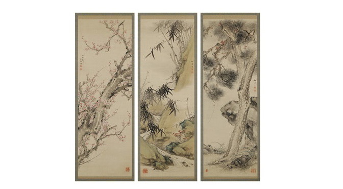 Imagem da gravura das plantas pinho, bambu e a flor de ameixeira em uma superfície de madeira.