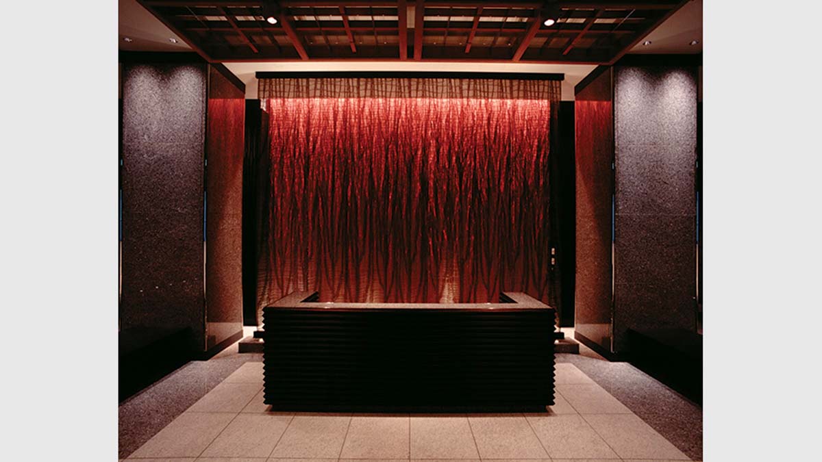Foto do saguão de entrada original do Mandarin Oriental, em Tóquio, projetado para evocar imagens de raízes de árvores, seguindo o conceito de design de ‘Madeira e Água’ do hotel, usando ricos tecidos de cor avermelhada concebidos por Sudō Reiko