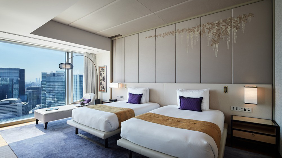 Quarto do Mandarin Oriental com duas camas grandes acolchoados brancos com detalhes em em marrom e almofadas azuis. 