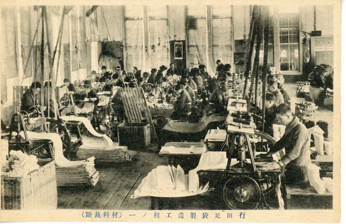 Cartão postal que mostra maquinário sendo utilizado para cortar material durante o processo de fabricação em uma fábrica 'tabi'.