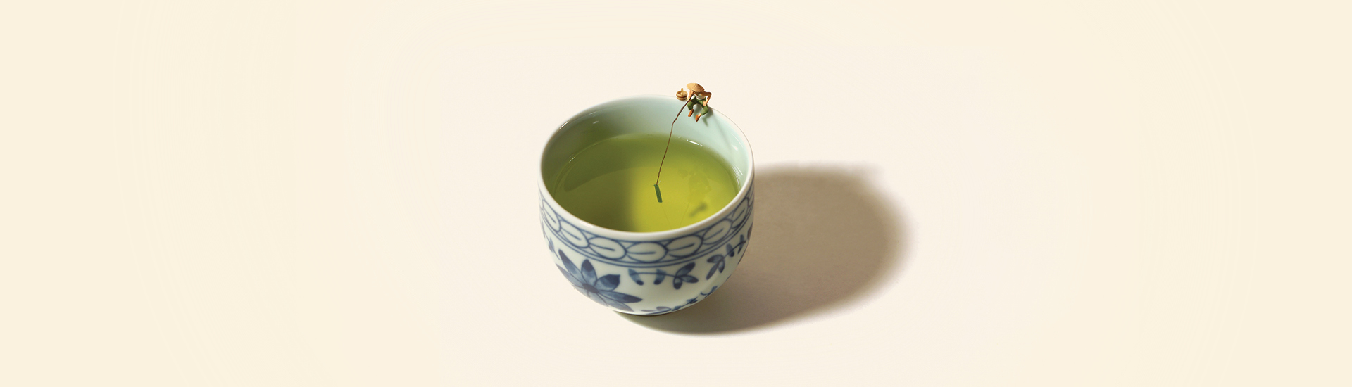 Fotografia de Tatsuya Tanaka, de xícara de chá verde com miniatura de homem pescando.