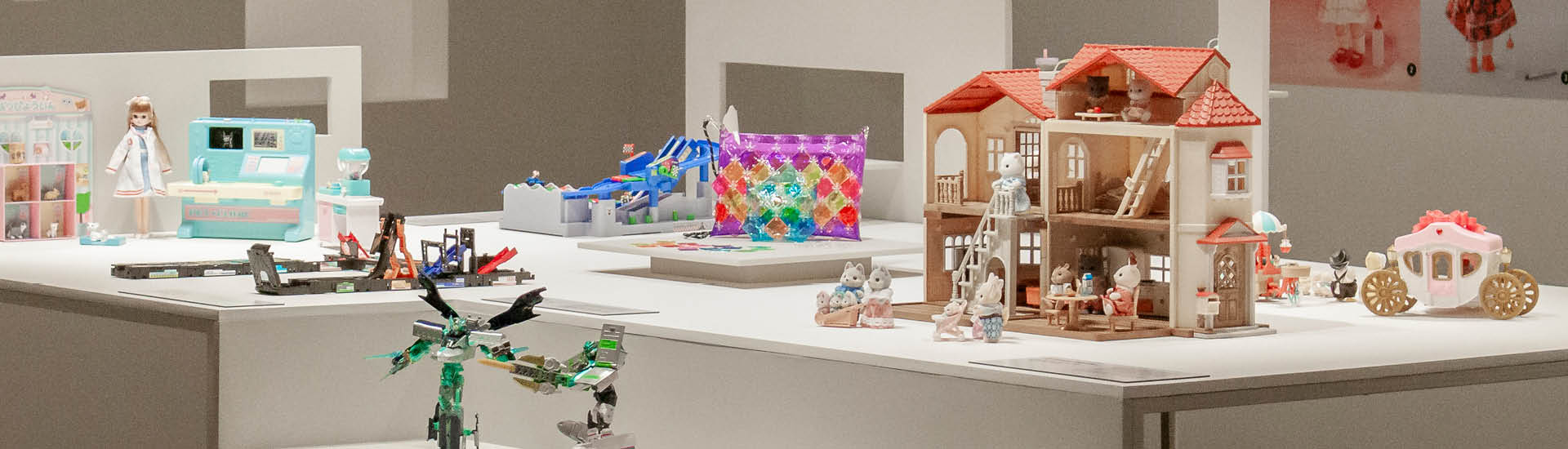 Brinquedos expostos em mesas brancas na exposição 'Doshin: os encantos dos brinquedos japoneses'