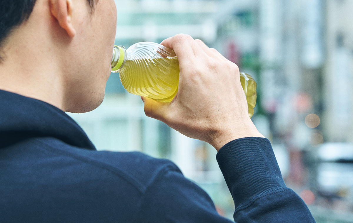 Foto de uma pessoa bebendo chá verde na garrafa pet
