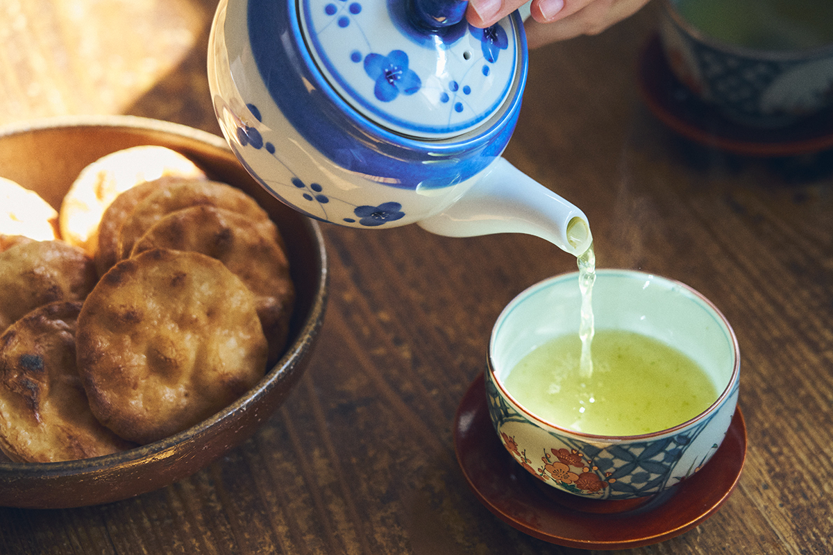 Foto detalhe de um bule japonês servindo chá verde ao lado de um prato com "senbei" biscoito japonês